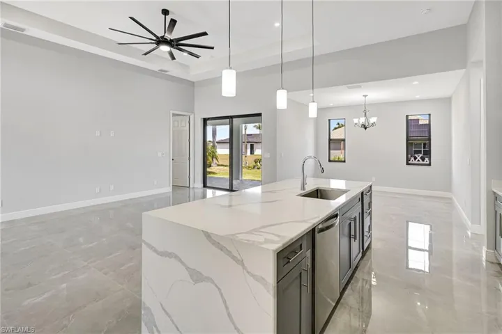 Kitchen with pendant lighting, light stone countertops, a kitchen island with sink, stainless steel dishwasher, and open floor plan