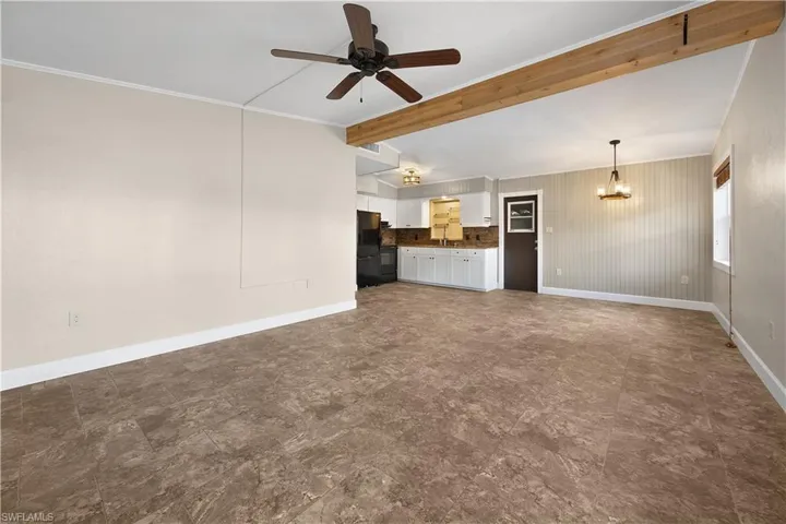 Unfurnished living room featuring ceiling fan, vaulted ceiling with beams, ornamental molding, and suspended lighting