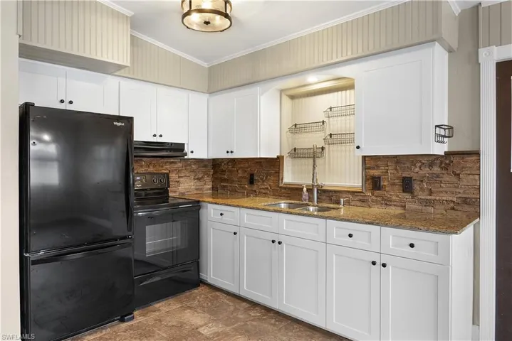 Kitchen with black appliances, crown molding, dark stone countertops, white cabinetry, and decorative backsplash