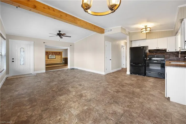 Kitchen featuring black appliances, crown molding, open floor plan, white cabinetry, and tasteful backsplash