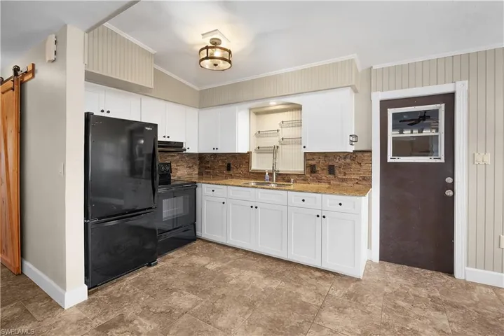 Kitchen featuring black appliances, crown molding, tasteful backsplash, white cabinets, and light stone countertops