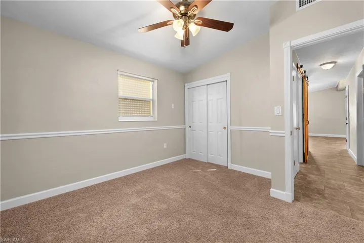 Unfurnished bedroom featuring carpet floors, ceiling fan, a barn door, a closet, and vaulted ceiling