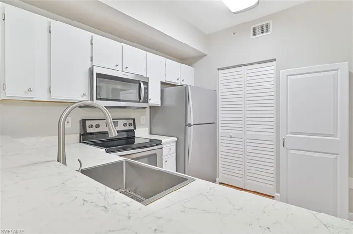Kitchen featuring light stone countertops, white cabinets, and stainless steel appliances