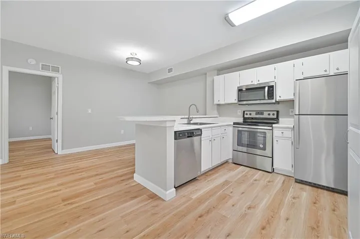 Kitchen with sink, appliances with stainless steel finishes, kitchen peninsula, and light wood-type flooring