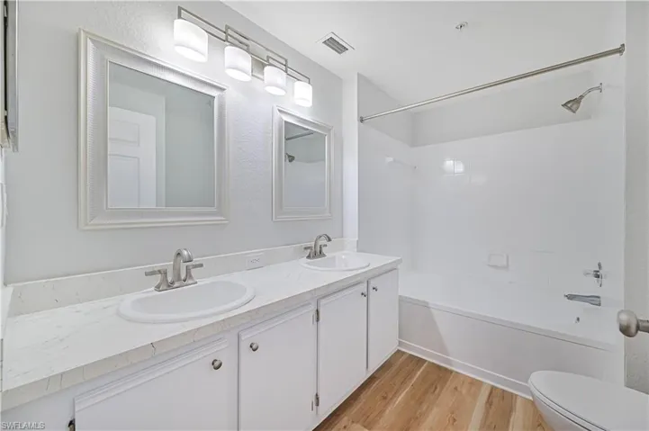 Full bathroom with wood-type flooring, toilet, dual vanity, and shower / washtub combination