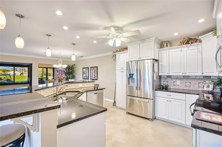 Kitchen with stainless steel appliances, white cabinets, a large island, a breakfast bar, and dark stone countertops