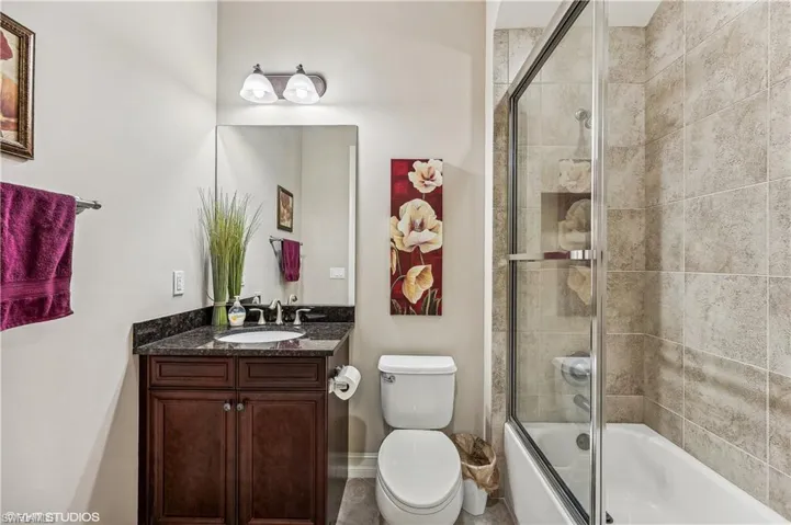 Full bathroom with vanity, shower / bath combination with glass door, and toilet