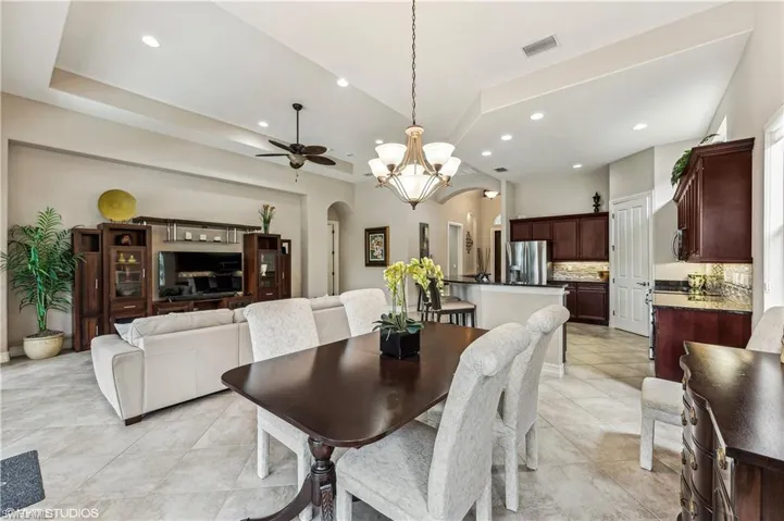 Tiled dining space featuring ceiling fan with notable chandelier and a tray ceiling