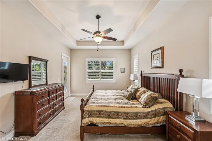 Bedroom with light carpet, ceiling fan, and a raised ceiling