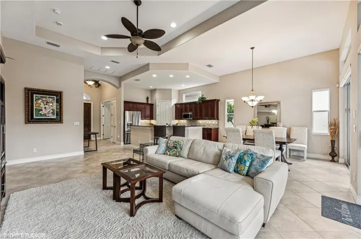 Tiled living room with ceiling fan with notable chandelier, a raised ceiling, and a towering ceiling
