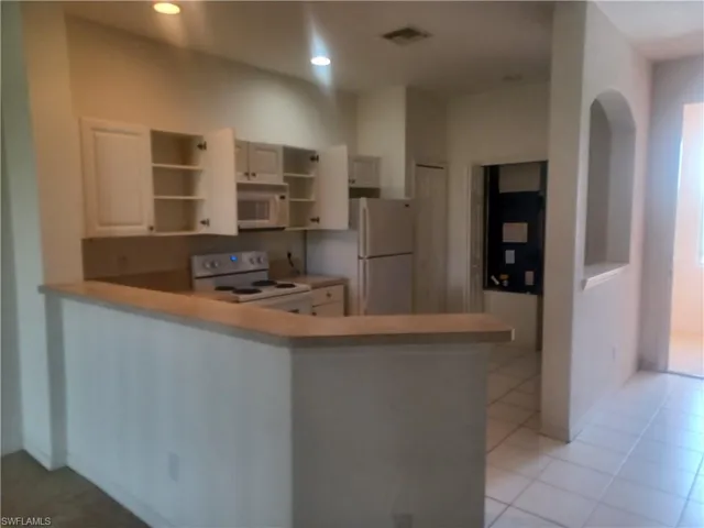 Kitchen featuring white appliances, light countertops, a peninsula, light tile patterned floors, and open shelves