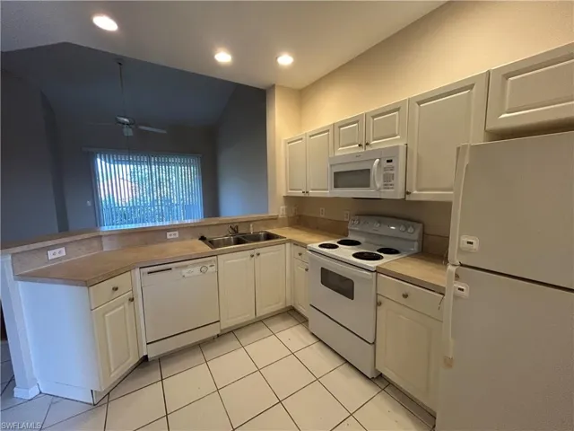 Kitchen featuring white appliances, a peninsula, a ceiling fan, light countertops, and light tile patterned floors