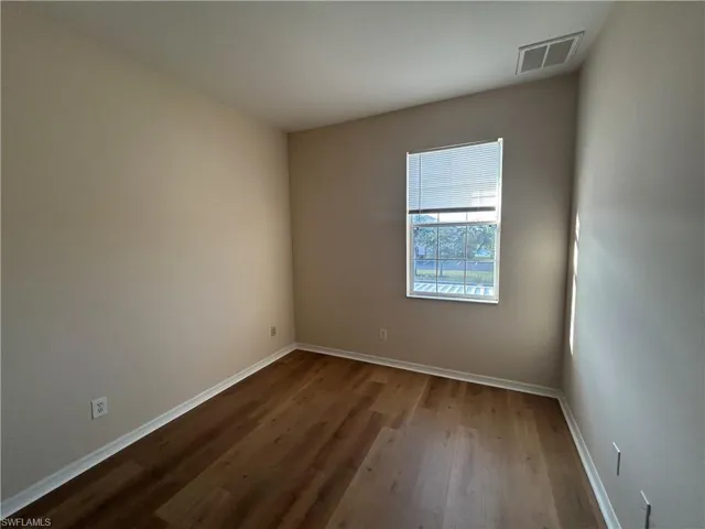 Spare room featuring dark wood-style flooring and baseboards