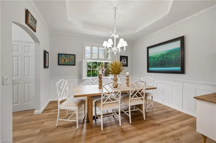 Dining area with crown molding, a chandelier, arched walkways, light wood-style floors, and a tray ceiling