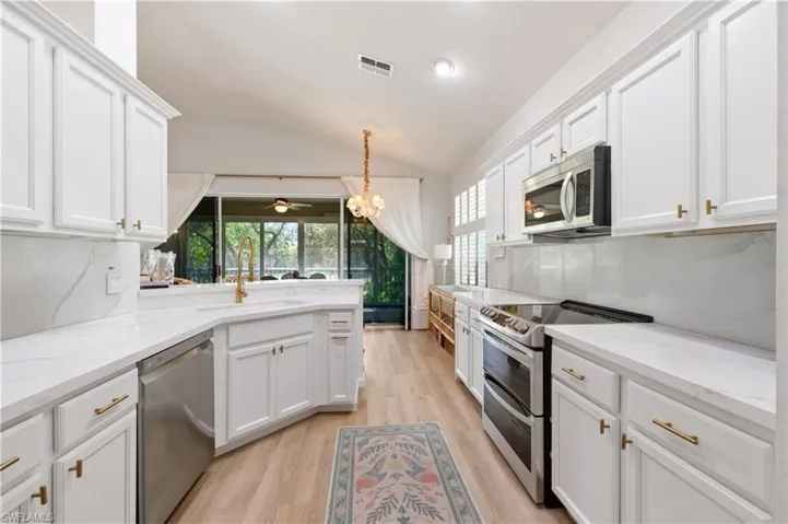 Kitchen featuring stainless steel appliances, lofted ceiling, white cabinets, a peninsula, and light wood-style flooring