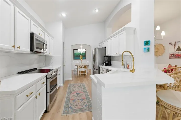 Kitchen featuring stainless steel appliances, a peninsula, arched walkways, light wood finished floors, and white cabinets