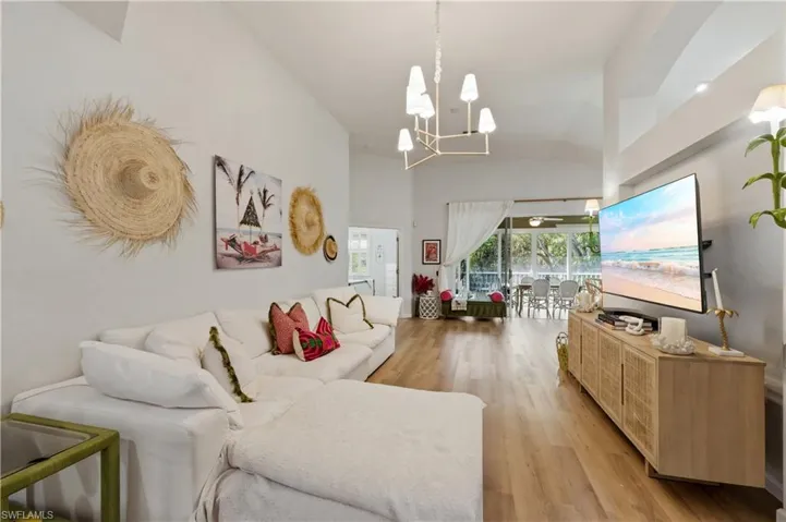 Living room featuring light wood-type flooring, hanging lights, and vaulted ceiling