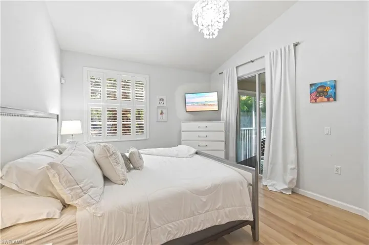 Bedroom with vaulted ceiling, access to exterior, light wood-style flooring, and hanging lights