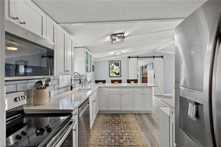 Kitchen with white cabinets, a barn door, light hardwood / wood-style floors, appliances with stainless steel finishes, and kitchen peninsula