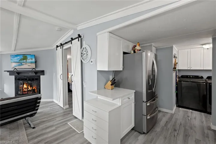 Kitchen featuring white cabinetry, crown molding, washer and clothes dryer, a barn door, and light hardwood / wood-style floors