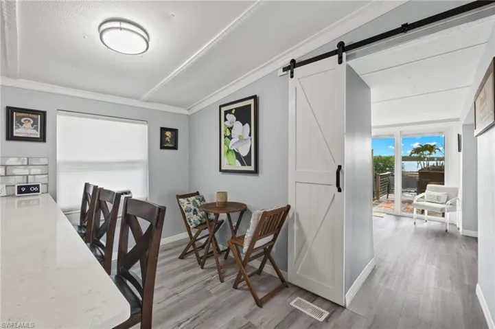 Dining room with light wood-type flooring, crown molding, and a barn door