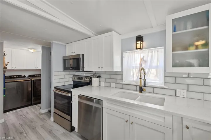 Kitchen featuring stainless steel appliances, washing machine and clothes dryer, sink, light wood-type flooring, and white cabinetry