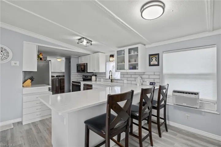 Kitchen with white cabinetry, kitchen peninsula, light stone countertops, appliances with stainless steel finishes, and a kitchen bar