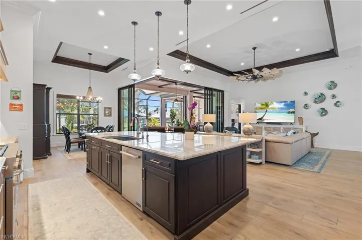 Kitchen featuring pendant lighting, a center island with sink, a raised ceiling, sink, and appliances with stainless steel finishes