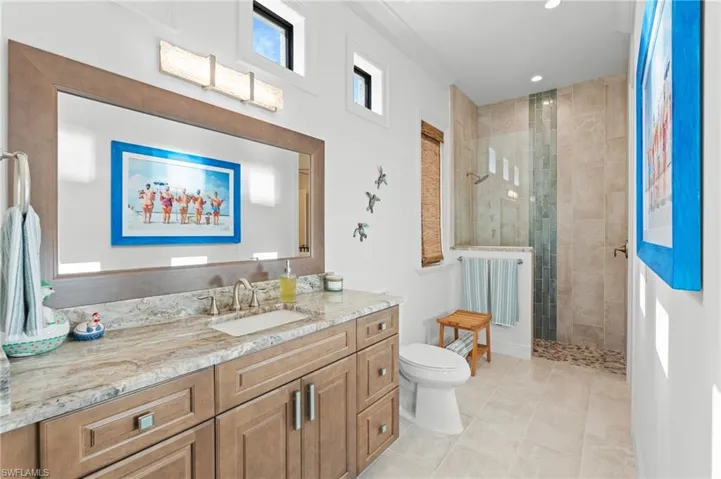 Bathroom with ornamental molding, vanity, tiled shower, tile patterned flooring, and toilet