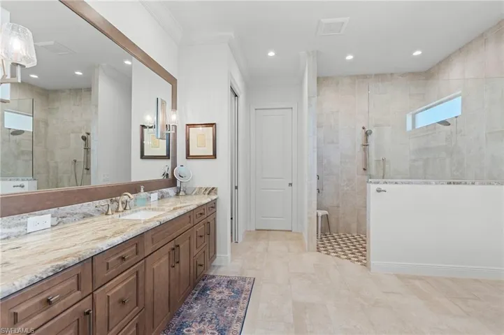 Bathroom featuring a tile shower, vanity, and crown molding