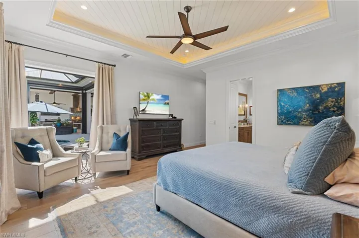 Bedroom featuring ceiling fan, ornamental molding, connected bathroom, a tray ceiling, and light hardwood / wood-style floors