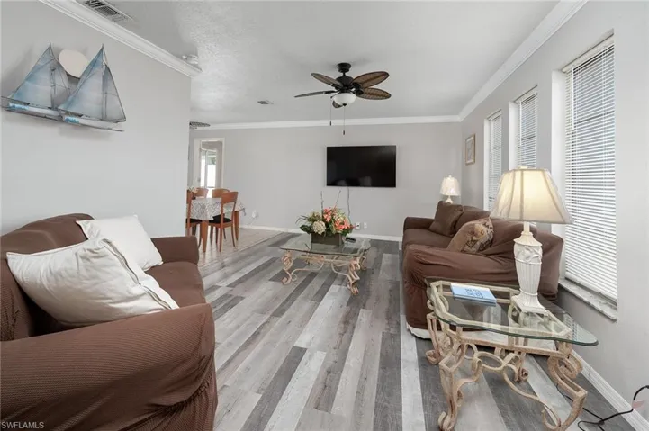 Living room with crown molding, a ceiling fan, and wood looking floors