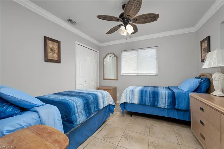 Bedroom with crown molding, a ceiling fan, light tile patterned floors, and a closet