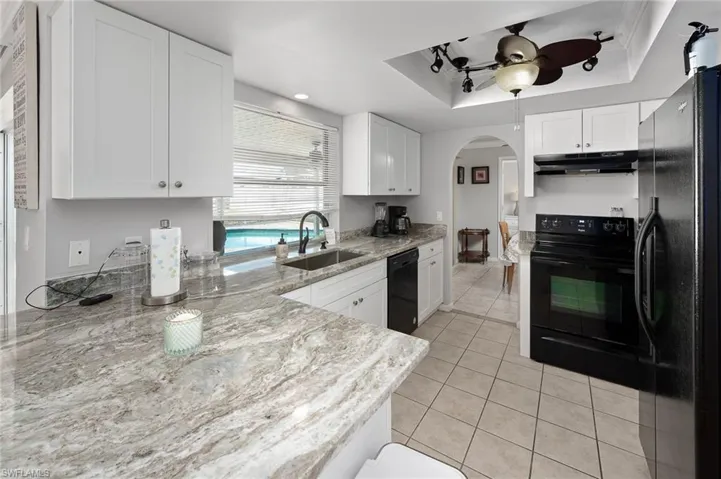 Kitchen featuring black appliances, light tile patterned flooring, white cabinets, and a ceiling fan