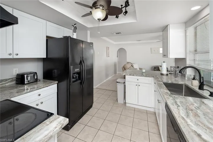 Kitchen featuring a tray ceiling, a peninsula, black appliances, and ceiling fan