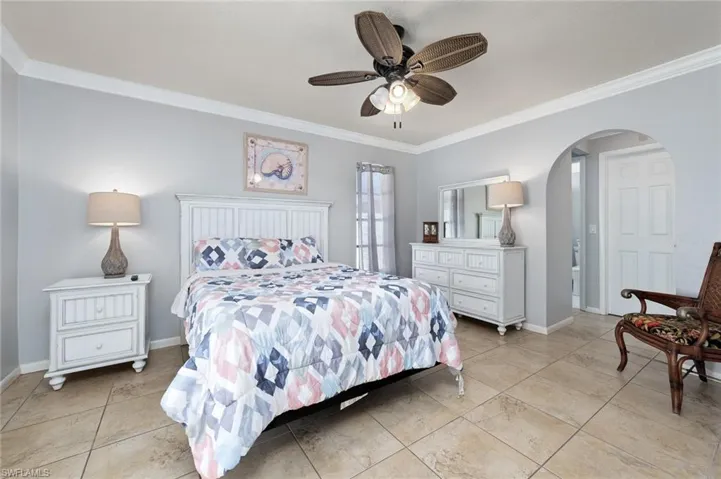 Primary bedroom featuring ornamental molding, arched walkways, ceiling fan, and tile floors
