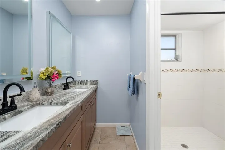 Bathroom featuring double vanity, light tile patterned floors, and a shower stall