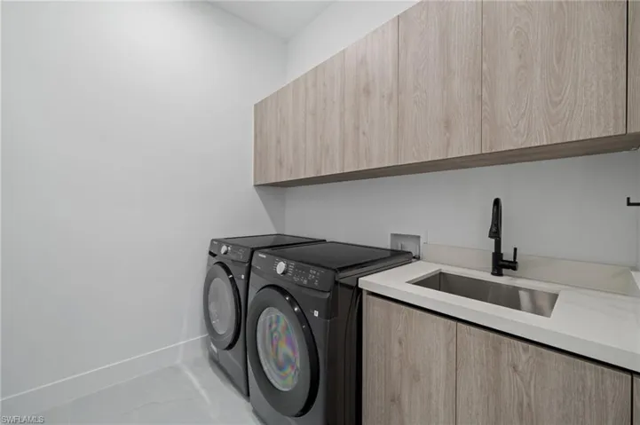Laundry area featuring independent washer and dryer, light tile patterned flooring, and cabinet space