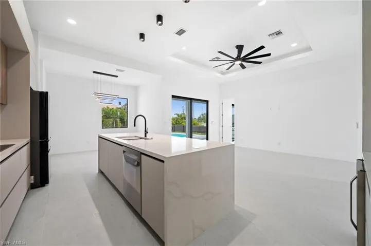 Kitchen with modern cabinets, a tray ceiling, an island with sink, light stone countertops, and recessed lighting