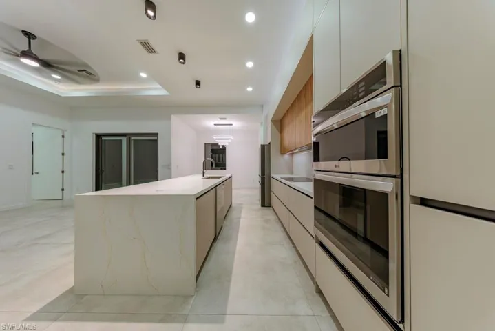 Kitchen with modern cabinets, stainless steel appliances, a large island, light stone countertops, and a raised ceiling