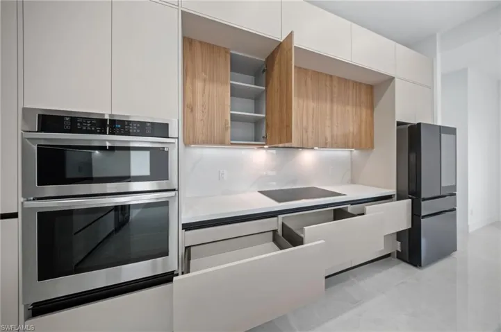 Kitchen featuring modern cabinets, black appliances, open shelves, backsplash, and light countertops