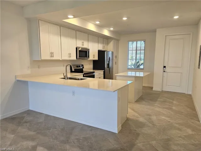 Kitchen featuring white cabinets, a peninsula, a center island, stainless steel appliances, and recessed lighting