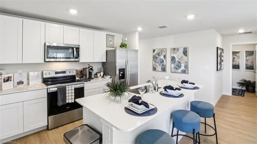 Model home. Kitchen featuring stainless steel appliances, a breakfast bar, light wood-style flooring, an island with sink, and white cabinets