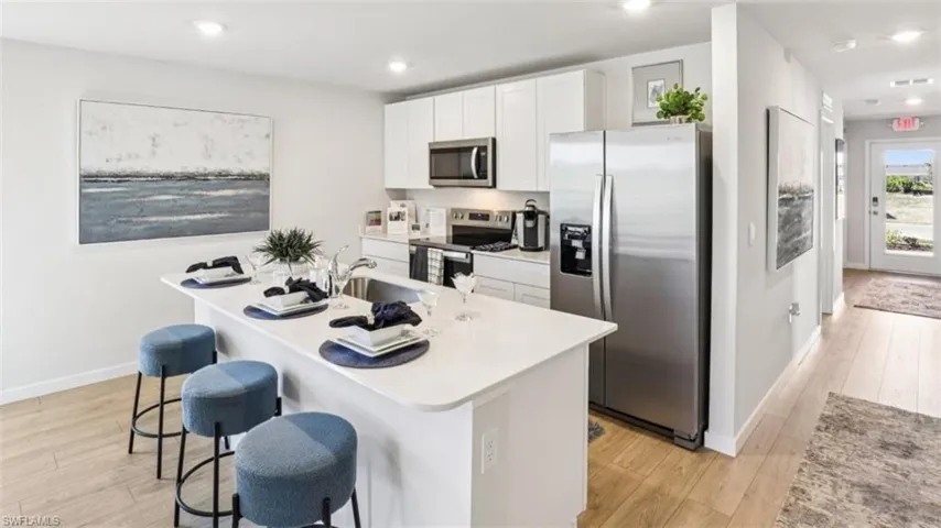 Model home. Kitchen featuring stainless steel appliances, white cabinetry, light wood finished floors, a kitchen breakfast bar, and an island with sink