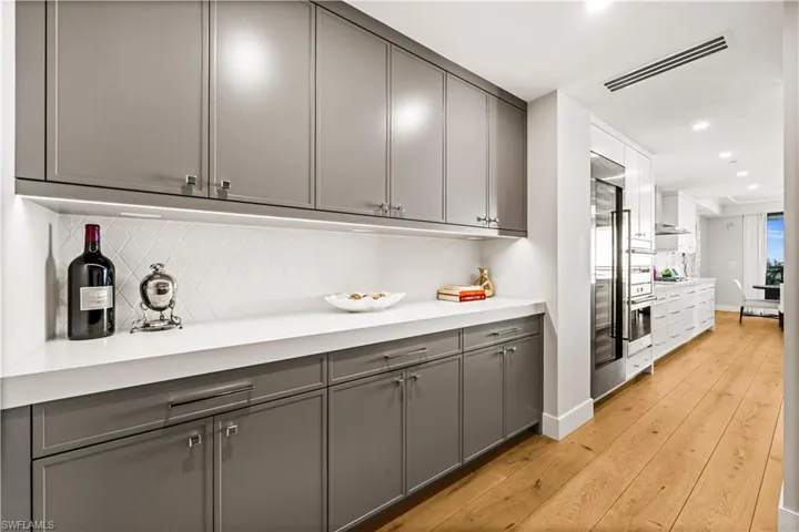 Bar area with gray cabinetry, light wood-type flooring, recessed lighting, stainless steel built in fridge, and tasteful backsplash