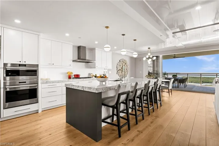 Kitchen with white cabinetry, a breakfast bar, decorative light fixtures, a large island with sink, and light wood-type flooring