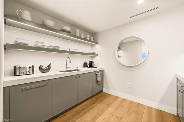 Bar area with gray cabinets, light wood-style floors, and open shelves