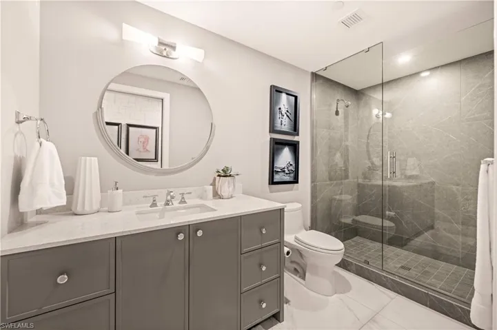 Full bath with vanity, a marble finish shower, and light marble finish floors