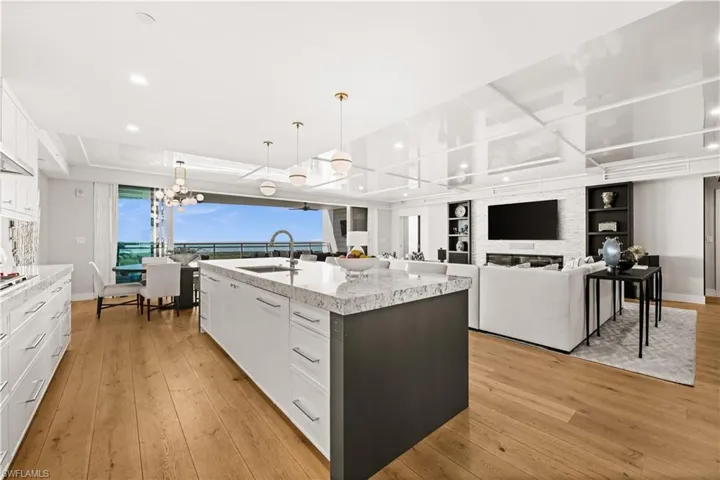Kitchen featuring white cabinets, decorative light fixtures, light wood-style flooring, open floor plan, and a center island with sink