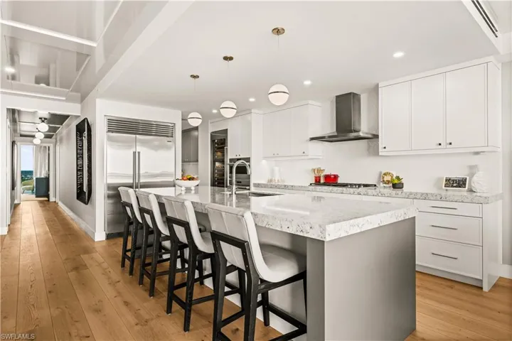 Kitchen featuring white cabinetry, light wood-style floors, decorative light fixtures, a kitchen breakfast bar, and a large island